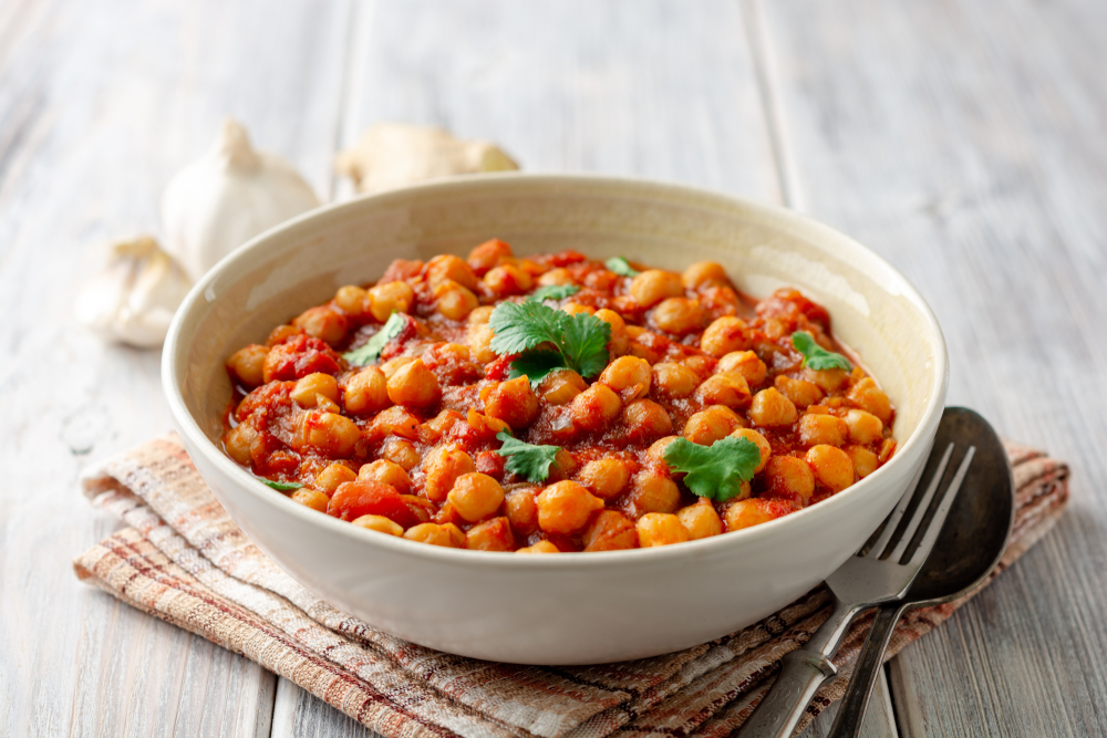 A bowl with chickpea curry inside with a spoon and fork next to it.